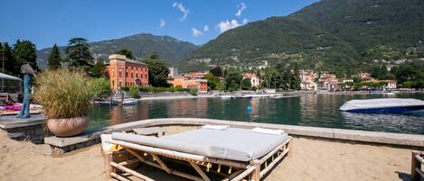 A beach with a lounge chair, a potted plant, and a water body with boats.