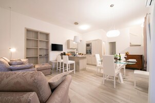 Un soggiorno moderno con un divano, un'area pranzo con sedie, una cucina con televisore e una scala.