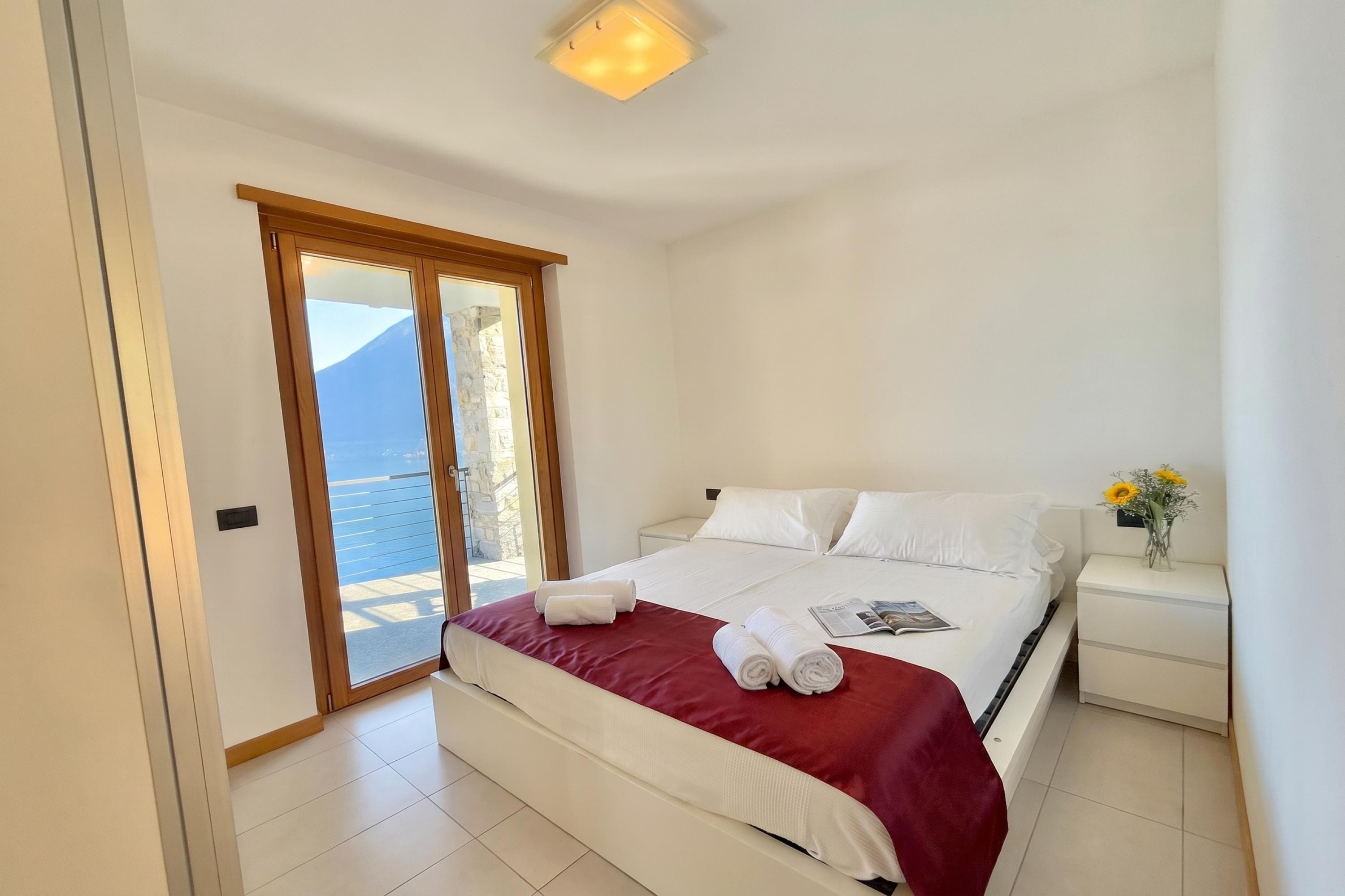 Une chambre à coucher comprenant un lit, une table de chevet, une fenêtre donnant sur un paysage agréable et une porte menant à un espace extérieur.