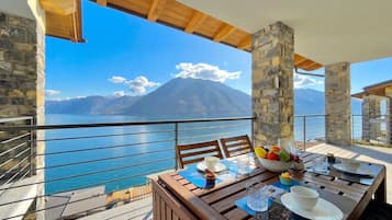 Un balcon avec une table dressée pour le dîner, offrant une vue sur un plan d’eau et des montagnes.