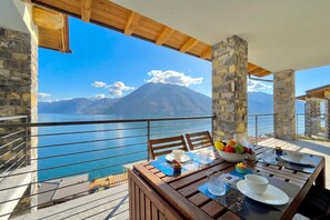 Un balcon avec une table dressée pour le dîner, offrant une vue sur un plan d’eau et des montagnes.