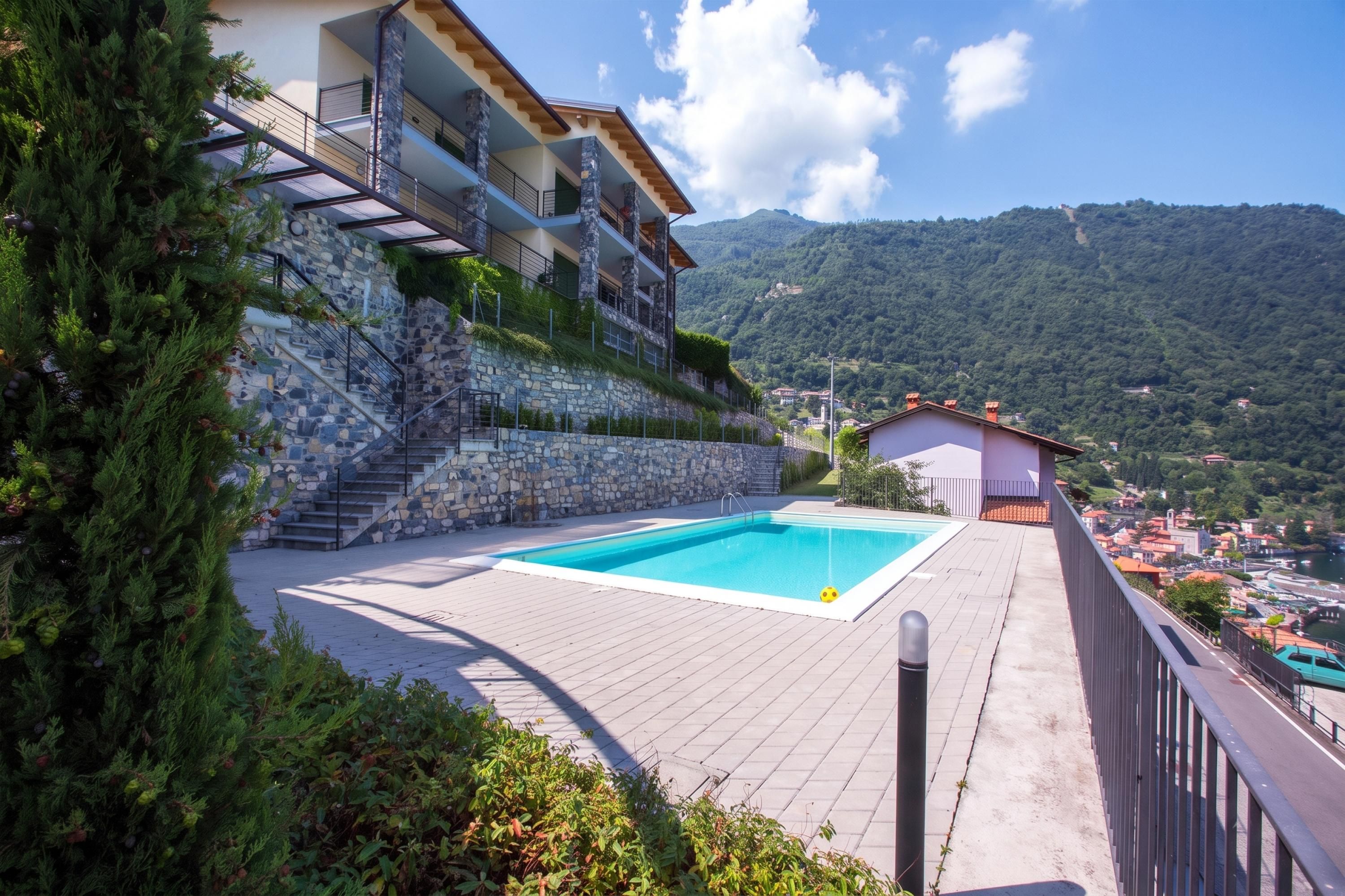 A poolside view of a multi-story building with a stone facade, a staircase, and a view of a mountainous landscape.