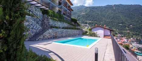 A poolside view of a multi-story building with a stone facade, a staircase, and a view of a mountainous landscape.
