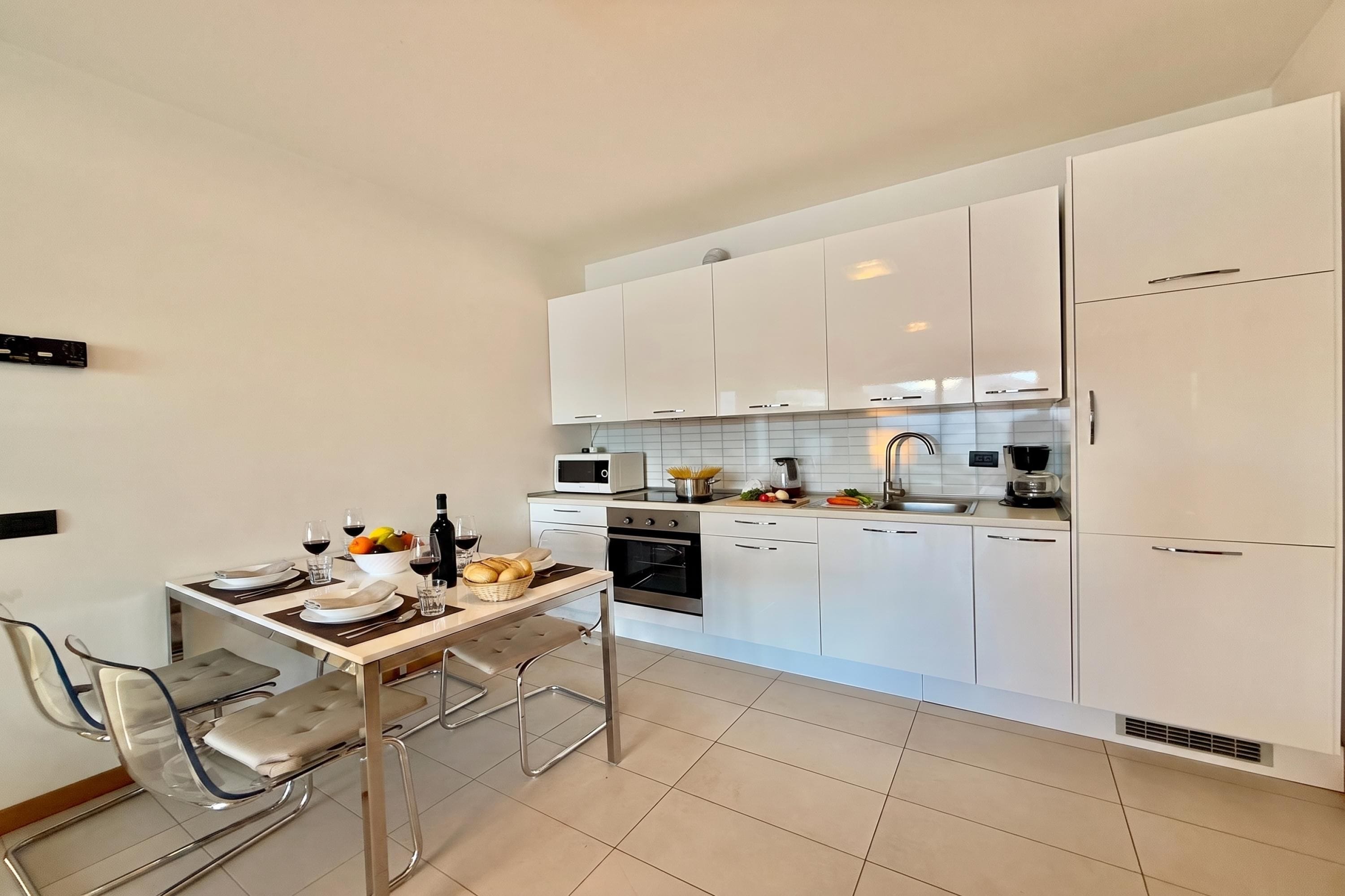Una cocina moderna con armarios blancos, una mesa de comedor con sillas y un horno empotrado.