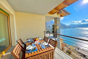 Un balcón con una mesa de madera dispuesta para comer, una vista despejada de un lago y montañas, y un pilar de piedra.