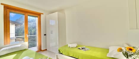 Quarto com duas camas, um guarda-roupa, uma janela com vista e um vaso de flores.
