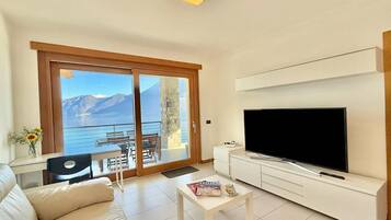 Una sala de estar moderna con un televisor grande, un sofá, una mesa de centro y un balcón con vistas a la montaña.