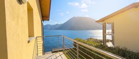 A balcony with a metal railing overlooking a body of water and mountains.