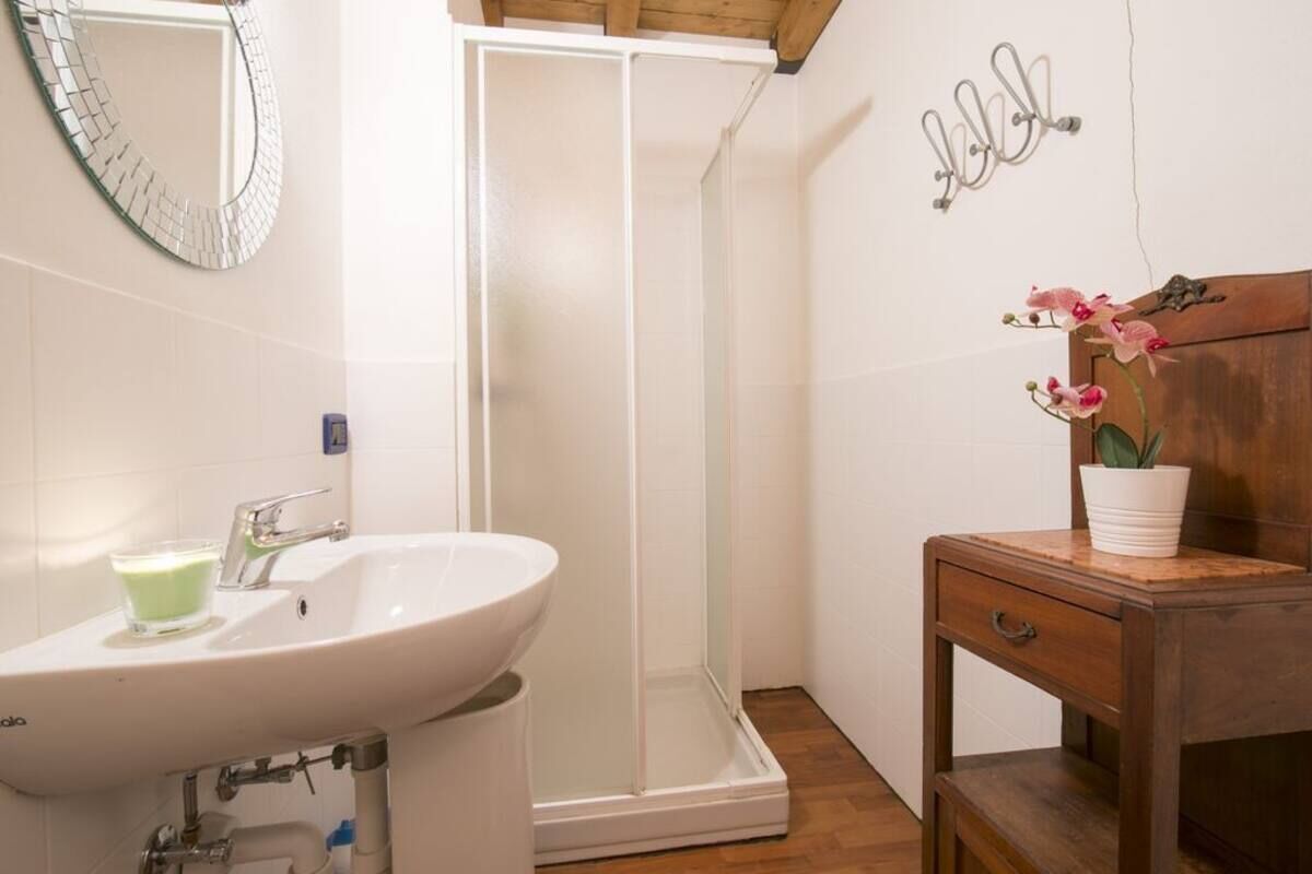 A bathroom with a white sink, a glass of green liquid, a wooden vanity, a potted orchid, and a shower enclosure.