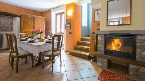 A dining area with a table set for four, a fireplace, and a staircase leading to another room. - Villa Frassi (Pianello del Lario)