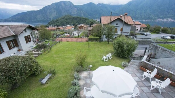 A residential area with a grassy backyard, a patio with a table and chairs, and a view of mountains and a lake. - Casa Simo Lenno (Tremezzina)