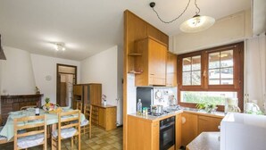 A kitchen with wooden cabinets, a stove, and a dining area with chairs and a table. - Casa Simo Lenno (Tremezzina)