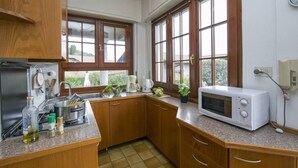A kitchen with wooden cabinets, a sink, a stove, a microwave, and a window with a view of greenery. - Casa Simo Lenno (Tremezzina)
