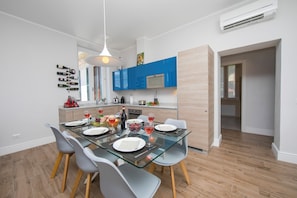 A modern kitchen with blue cabinets, a glass dining table, and a hanging wine rack.