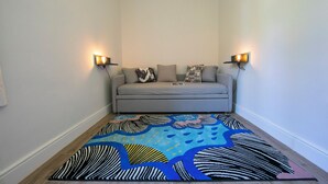 A small, cozy room with a grey sofa, two wall-mounted lamps, and a colorful abstract rug. - Casa Maria Menaggio (Menaggio)