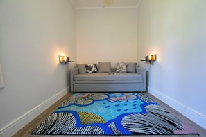 Una habitación pequeña y acogedora con un sofá gris, dos lámparas fijadas a la pared y una alfombra abstracta y colorida.