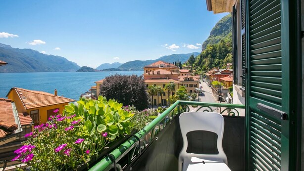 A balcony with a view of a lake, buildings, and mountains. - Casa Maria Menaggio (Menaggio)