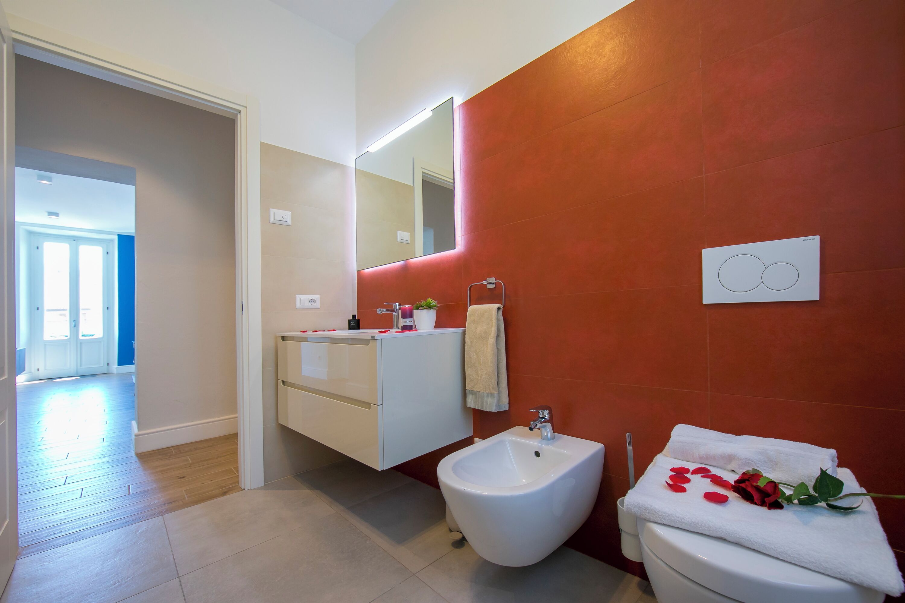 A modern bathroom with a bidet, a vanity with a mirror, and a red accent wall.