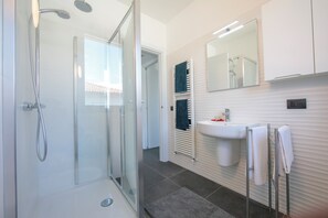 Casa de banho moderna com chuveiro envidraçado, lavatório branco e espelho em cima.