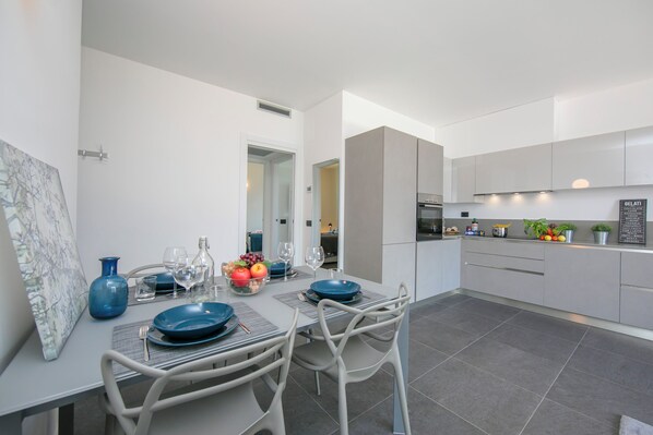 Een moderne keuken met grijze kastjes, een eethoek met een tafel gedekt voor twee personen, en een groot raam.