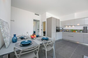 A modern kitchen with grey cabinets, a dining area with a table set for two, and a large window.