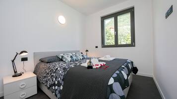 Een slaapkamer met een bed, een nachtkastje, een lamp, een raam en uitzicht op groen.