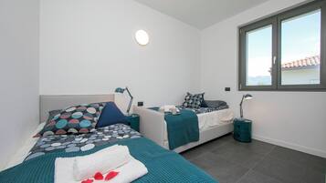 A modern bedroom with two beds, teal bedding, and bedside lamps.