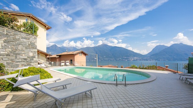 A swimming pool with lounge chairs, a stone wall, and a view of mountains. - Residence Romina Lakeview Apt. (San Siro)