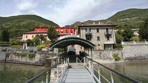 A bridge leading to a building labeled "ACQUASERIA" with a stone wall and greenery in the background. - Residence Romina Lakeview Apt. (San Siro)