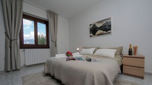 A bedroom with a bed, a bedside table with a bottle, a framed picture on the wall, and a window with curtains. - Sonenga Panoramic Terrace (Menaggio)