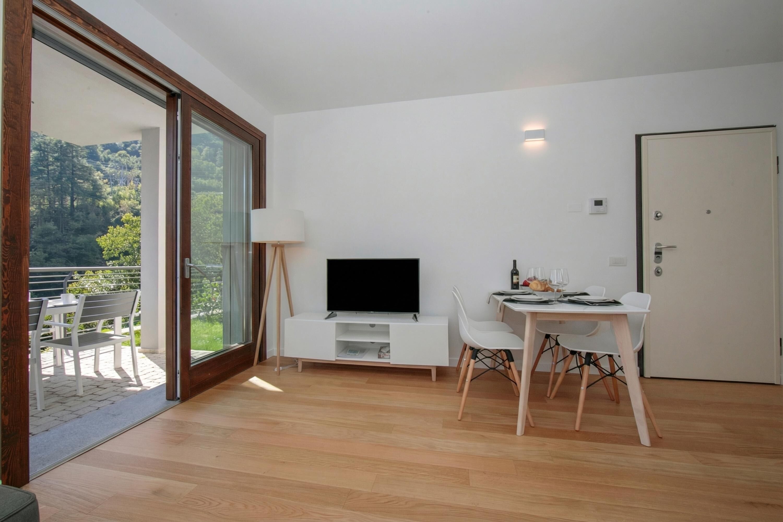 A modern room with a TV, dining table, chairs, and a sliding glass door leading to an outdoor area.