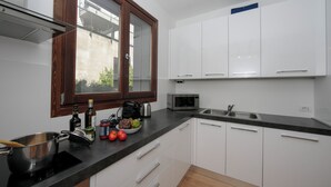 A modern kitchen with white cabinets, a black countertop, a microwave, and a window with a wooden frame. - Argegno Home (Argegno)