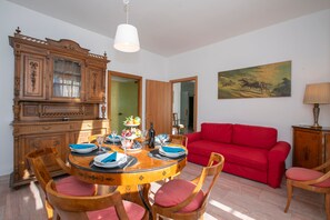A dining area with a wooden table set for four, surrounded by wooden chairs with red cushions. A red sofa is positioned against the wall, and a painting is visible above it. - La Casa del Vitt (Menaggio)