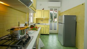A compact kitchen with yellow cabinets, a stainless steel refrigerator, and a gas stove. - La Casa del Vitt (Menaggio)