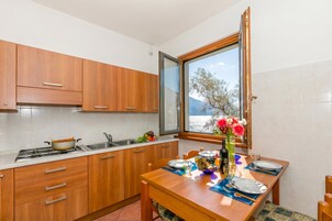 Uma cozinha com armários de madeira, uma mesa de jantar posta para dois e uma janela com vista para árvores e montanhas.