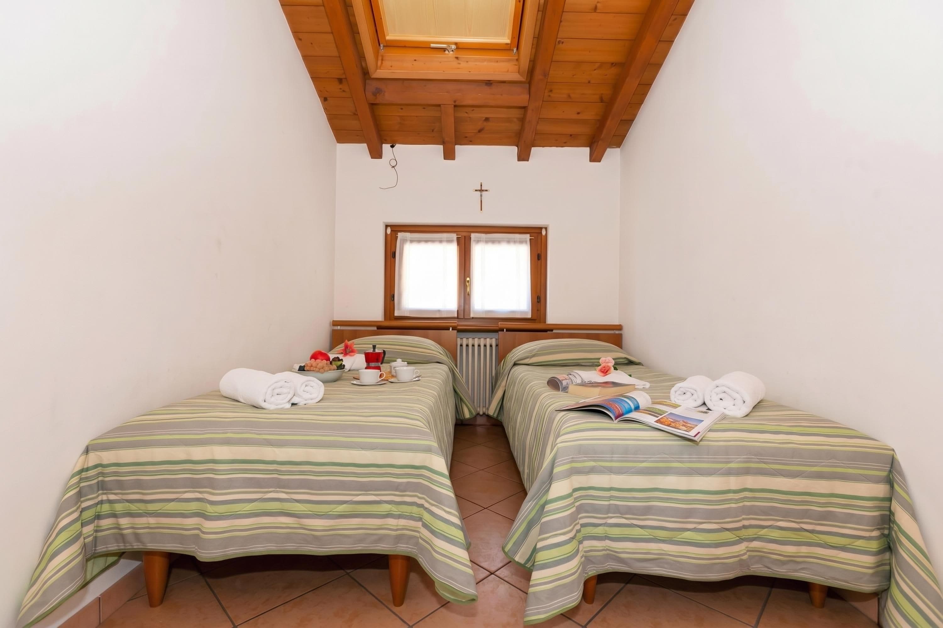 Una habitación pequeña y acogedora con dos camas individuales, techo de madera, ventana con cortinas y un radiador.