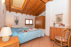 A bedroom with a bed, wooden wardrobe, and a desk with a lamp.