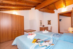 Habitación de hotel con dos camas, armario de madera, mesitas de noche, un espejo y un escritorio pequeño con silla.