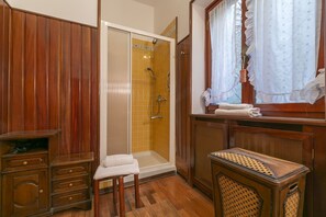 Un baño con paneles de madera, una ducha con azulejos amarillos, un banco de madera y una ventana con cortinas.