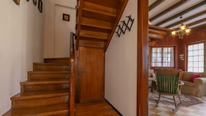 Una escalera de madera conduce a una habitación con piso a cuadros, una mecedora y un candelabro.
