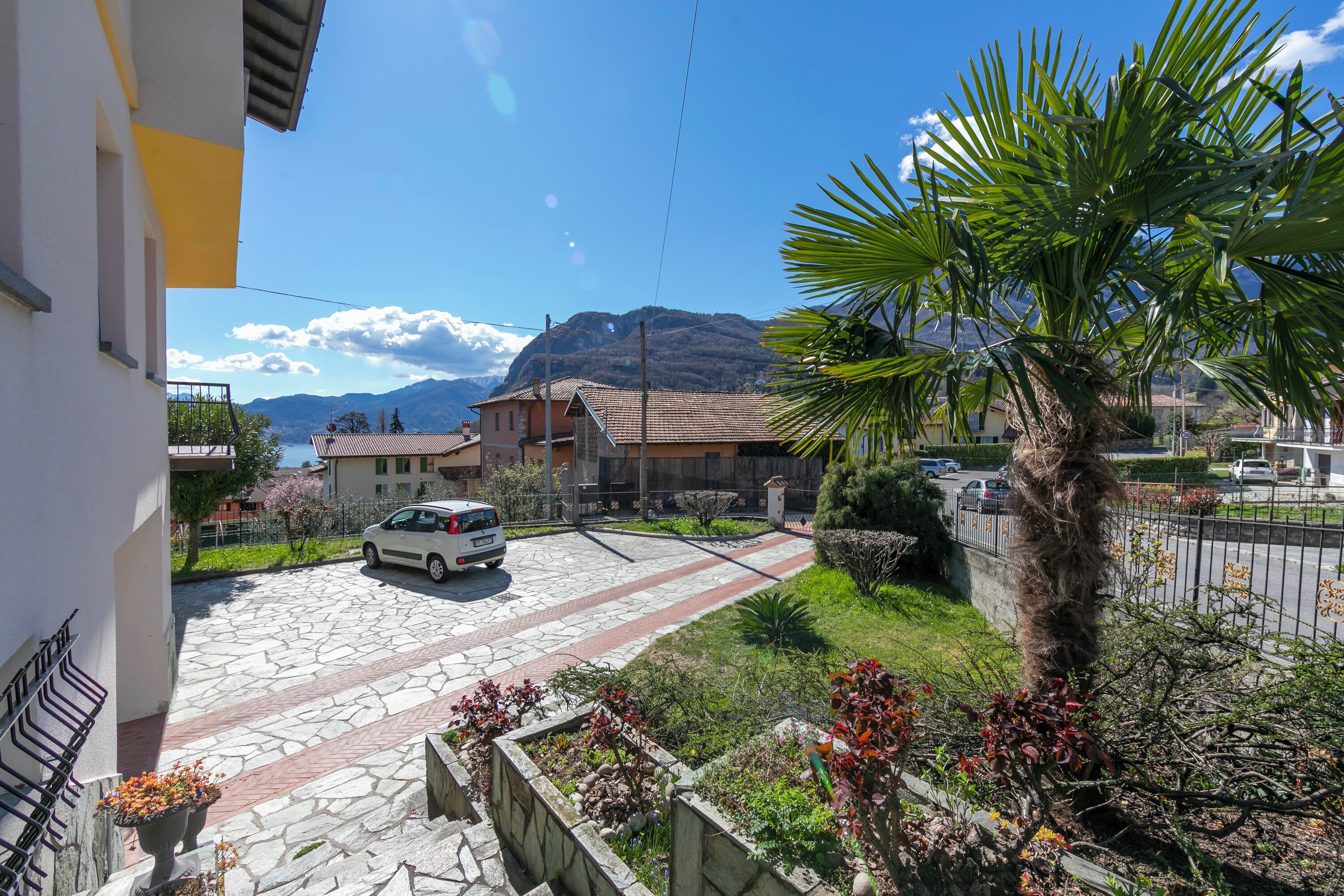 Uma rua residencial com um carro estacionado, um caminho de pedra e uma montanha ao fundo.