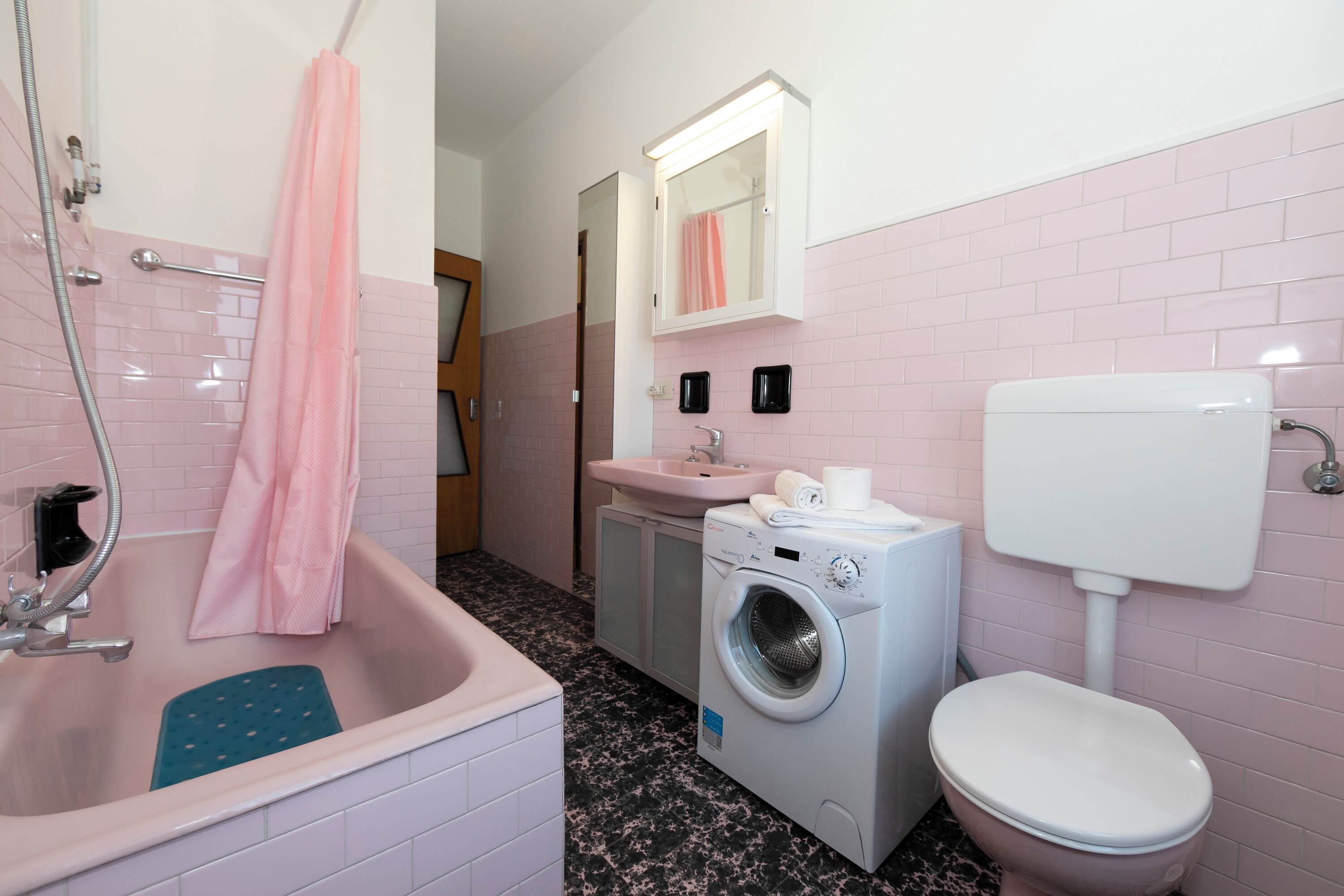 Casa de banho com lavatório, sanita, máquina de lavar roupa e zona de duche.