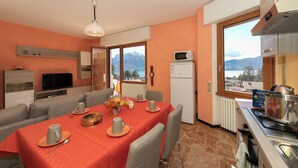 A dining area with a table set for four, a kitchen with a stove and microwave, and a view of mountains through the windows. - Il Panorama di Forster (Menaggio)