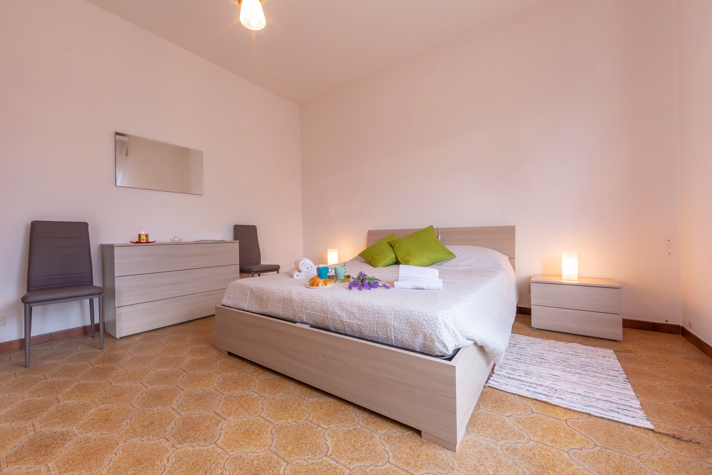 A bedroom with a bed, a dresser, a chair, a nightstand, and a mirror.