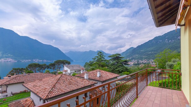 Un balcone con pavimento piastrellato e ringhiera in ferro battuto che si affaccia su un paesaggio montuoso con un lago.