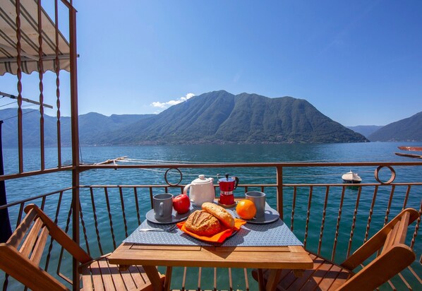 A table with breakfast items on a boat deck, overlooking a mountainous lake.