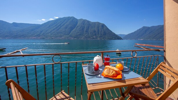 Een tafel met een maaltijd op een balkon met uitzicht op een meer met boten en bergen.