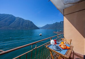 A balcony with a table set for breakfast, overlooking a calm lake and mountains.