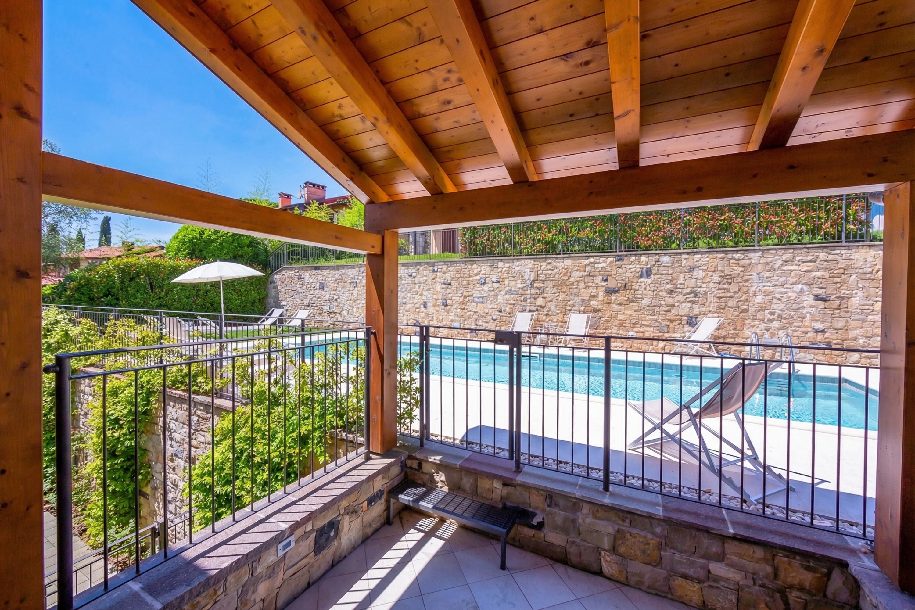 A covered outdoor area with a stone wall, a pool, and lounge chairs.