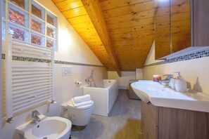 A bathroom with a bathtub, a sink, a toilet, and a window with blinds. - Como Lake Modern apartment Ulivi (Tremezzina)